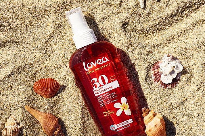 Editorial Lovea — ulei de plaja cu monoï asezat in nisip printre scoici si o stea de mare